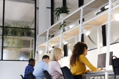 Group of busy concentrated creative colleagues in casual clothing sitting at tables with devices and working with papers in modern office